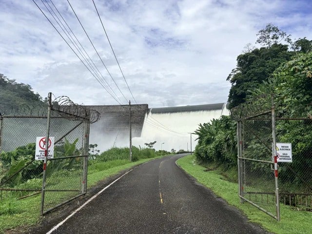 A road leads toward the dam between forested hills.