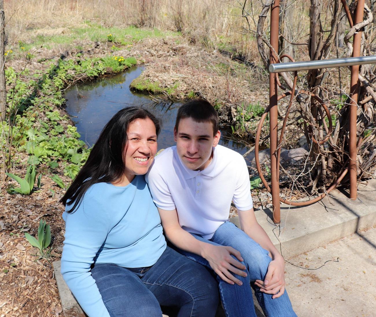 Margaret King and son Hudson Francour sitting by a creek, smiling